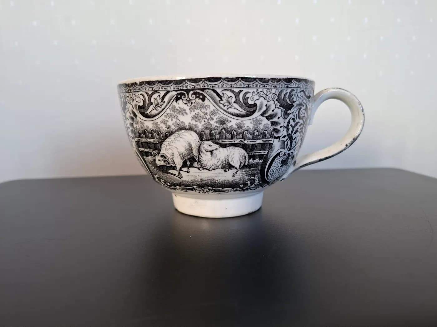 Tasse en faïence à décor imprimé noir : un bélier et une brebis devant une barrière, dans un cadre d'arabesques.