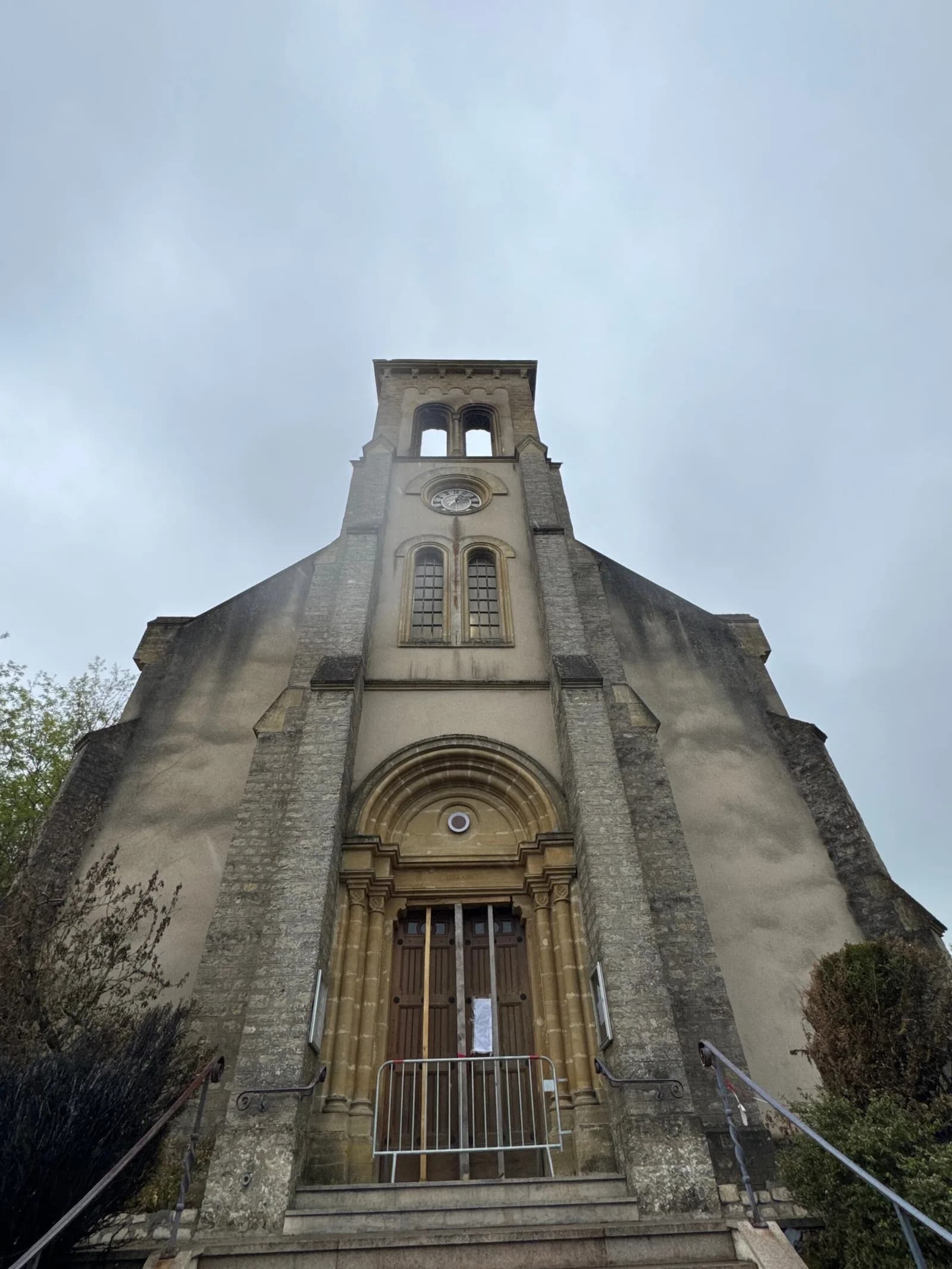 Façade d'une église en pierre avec un clocher, vue en contre-plongée sous un ciel gris.